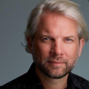 A professional headshot of Professor Andrew Briggs against a pale blue backdrop